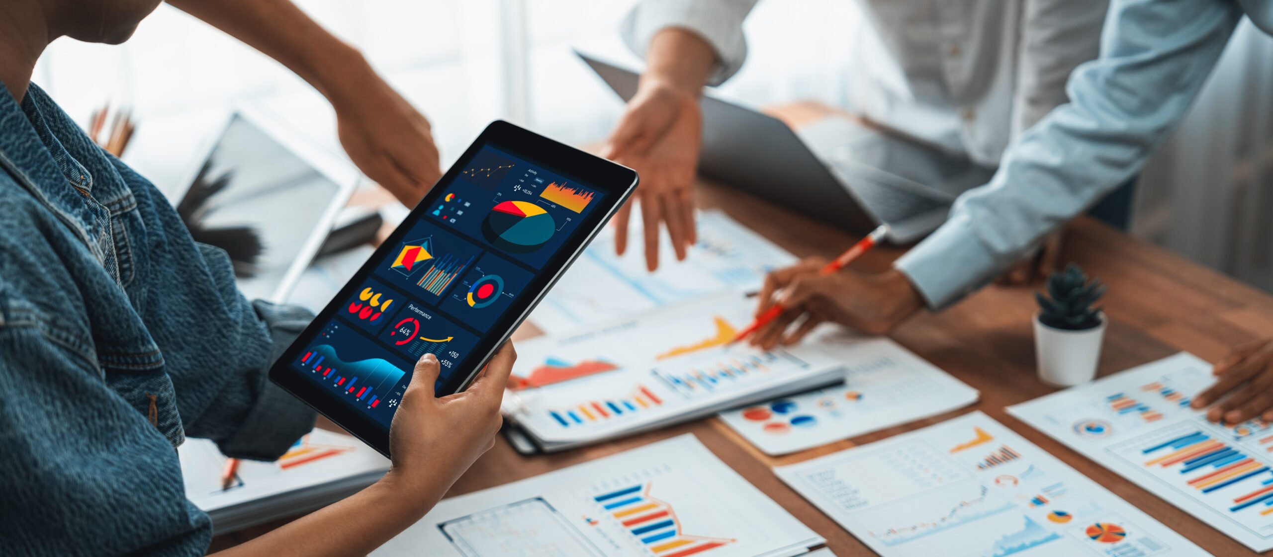 Analyst team utilizing BI Fintech to analyze financial report with tablet over paper on table and analyzing BI power dashboard display on tablet screen for business insight. Panorama shot. Scrutinize